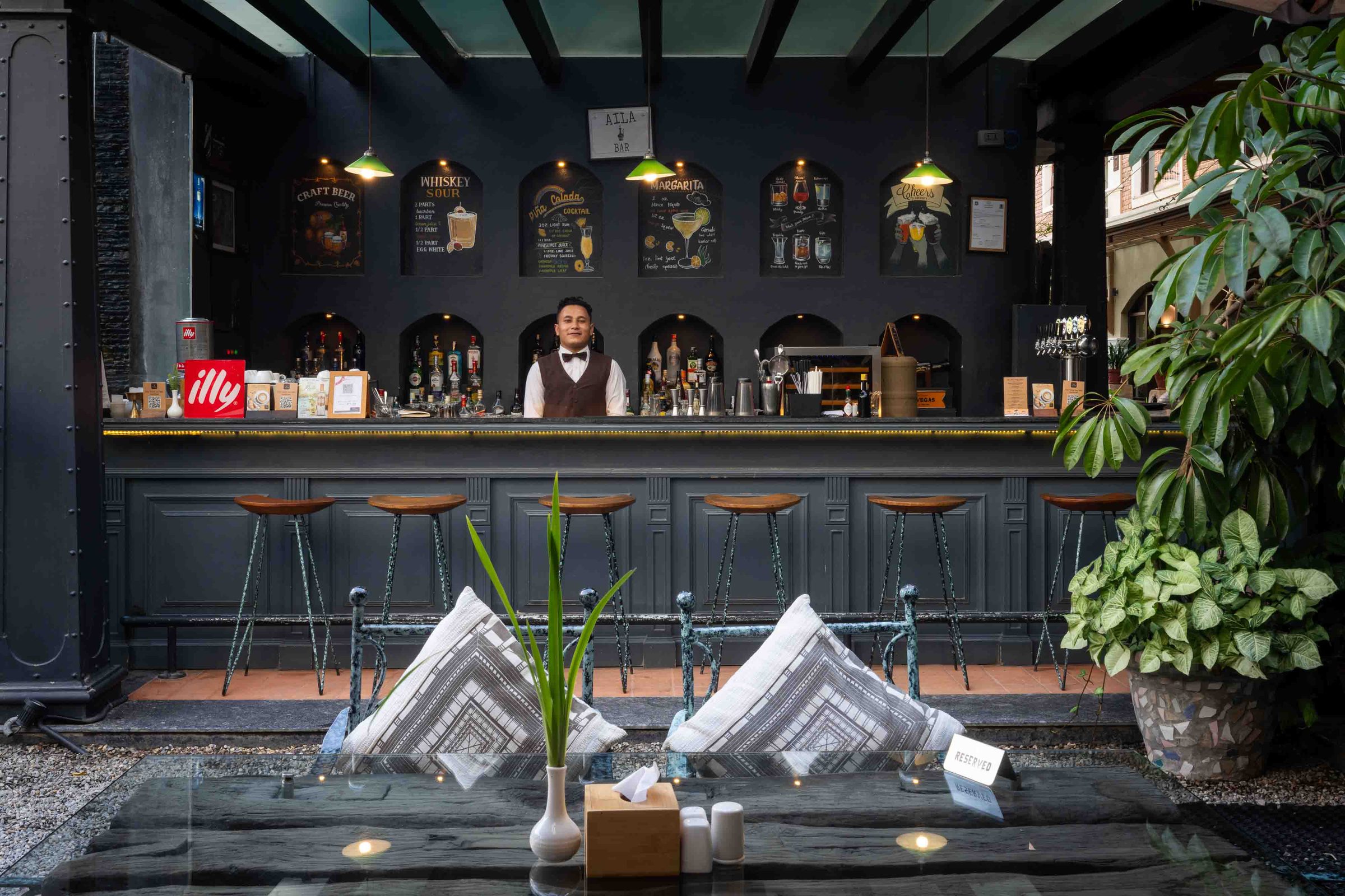 The Jharana Bar counter at dusk, a bartender behind the taps with timber stools and hand-chalked cocktail recipes above
