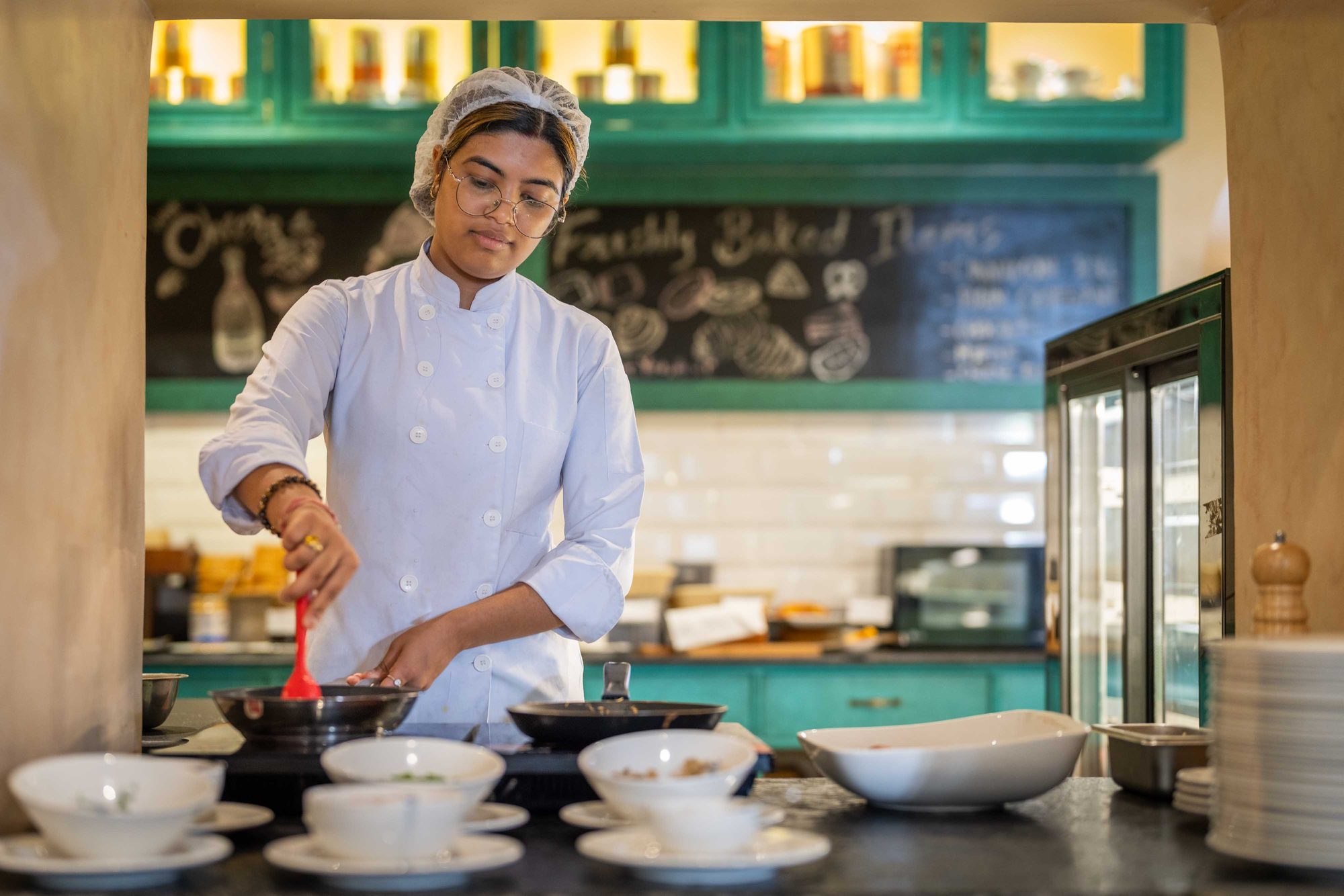 A chef finishing a dish at the Chiya Pasal counter beneath the chalked menu board