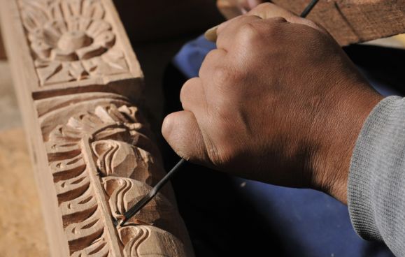 A craftsman’s hands chiselling a floral frieze into a timber beam at a Newari wood-carving workshop